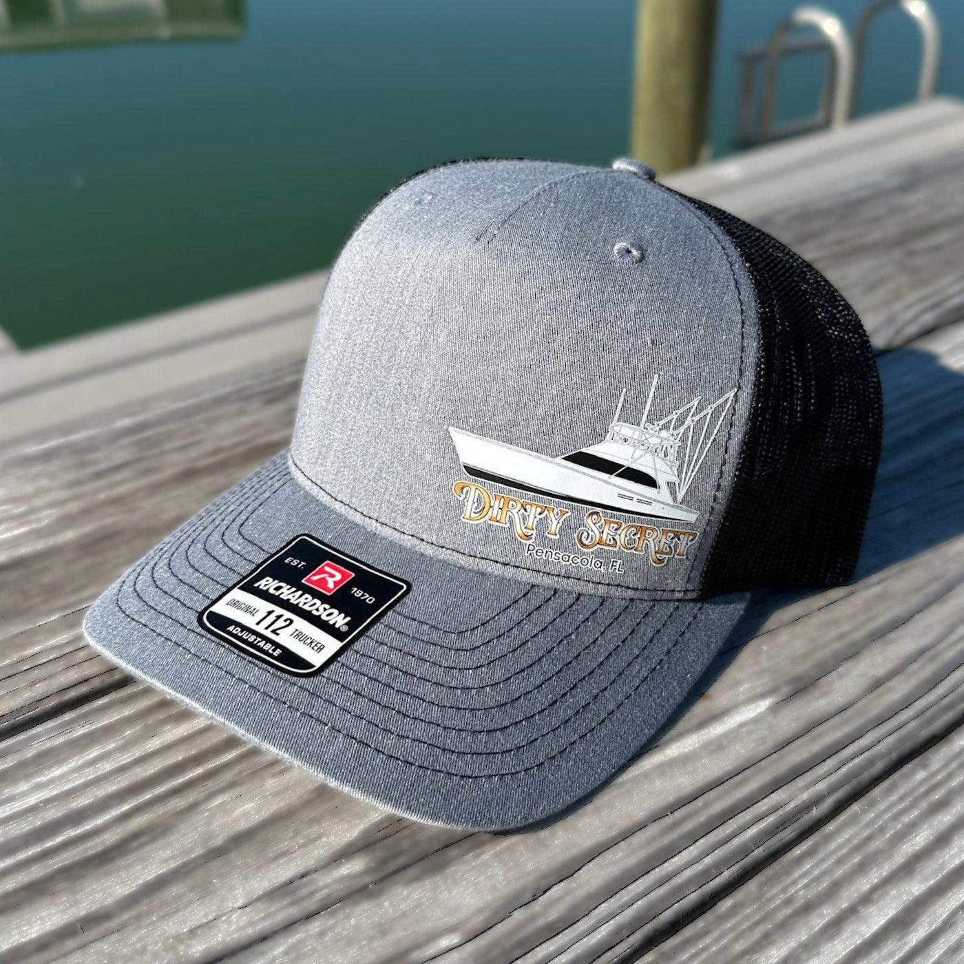 Gray cap with boat logo and text on a wooden surface by water